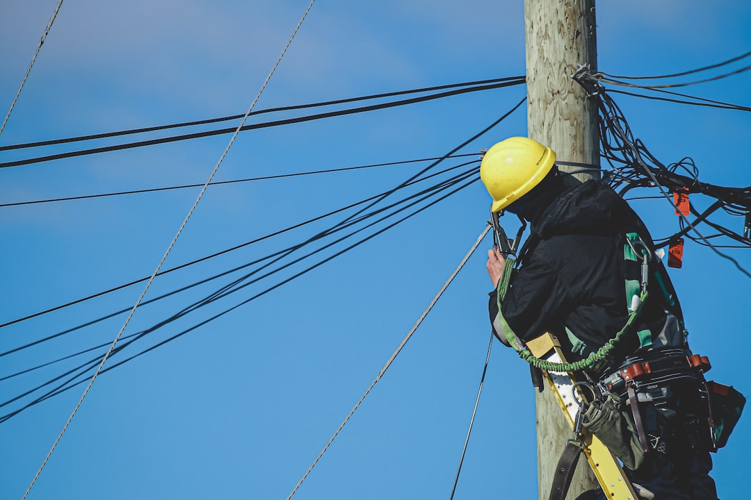 man-in-black-jacket-and-yellow-hard-hat-climbing-on-brown-wooden-post-during-daytime-4khklzujeyi